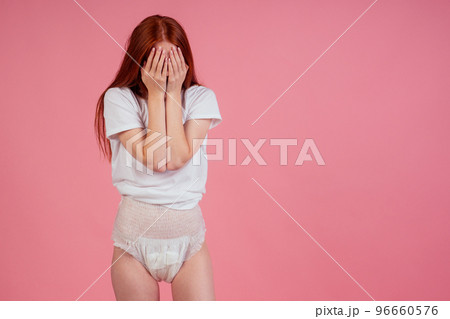 young amazed and surprised redhaired ginger woman wearing incontinence diaper in studio pink background.feeling shame and embarrassment 96660576