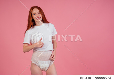 happy young redhaired ginger woman wearing incontinence diaper in studio pink background showimh thumbs up 96660578