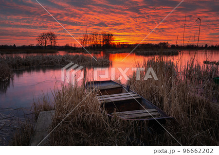 An old boat in the reeds on the lake shore and a beautiful sunset An old boat in the reeds on the lake shore and a beautiful sunset 96662202