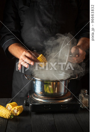 A professional chef cooks corn. Close-up of a cook is a hand while cooking in a restaurant kitchen. Vertical image 96663832
