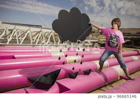 a cute kid in a pink t-shirt with a cat print plays among pink pipes with black clouds, rain, boats and paper planes against the blue sky in an industrial location. fashion style photoshoot a cute kid in a pink t-shirt with a cat print plays among pink pipes with black clouds, rain, boats and paper planes against the blue sky in an industrial location. fashion style photoshoot 96665146