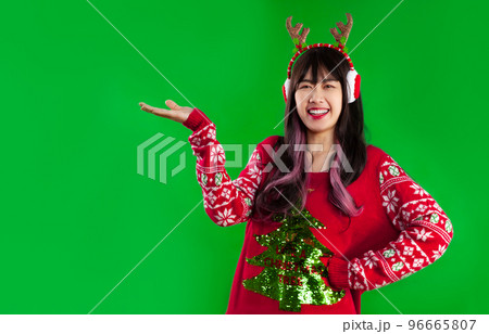 Young pretty asian woman in red sweater christmas theme wear reindeer horns headband posing hand pointing for your product of text on green screen background. Merry Christmas. 96665807