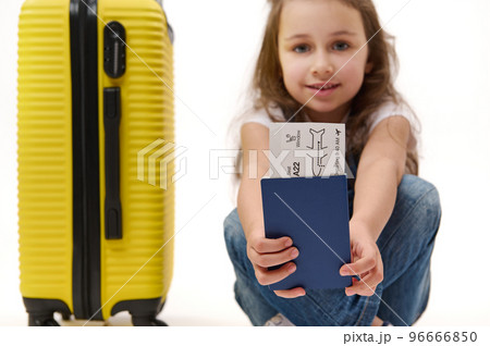 Details: boarding pass and identity documents for travel abroad in the hands of a blurred smiling little girl traveller with yellow suitcase, isolated over white background. Journey. Air flight trip Details: boarding pass and identity documents for travel abroad in the hands of a blurred smiling little girl traveller with yellow suitcase, isolated over white background. Journey. Air flight trip 96666850