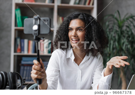 Attractive young multinational woman in white shirt taking selfie on her smart phone using stick. 96667378