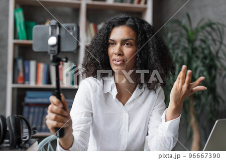 Attractive young multinational woman in white shirt taking selfie on her smart phone using stick. 96667390