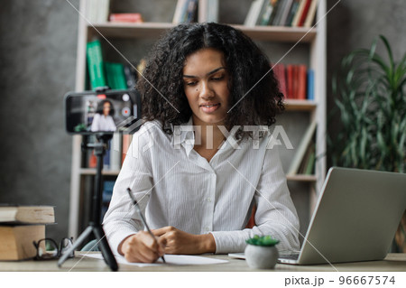 Charming multinational woman in white shirt talking with subscribers while writing report Charming multinational woman in white shirt talking with subscribers while writing report 96667574