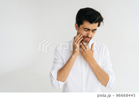 Studio portrait of sick man with closed eyes suffering from severe toothache, touching jaw with fingers trying to ease strong tooth pain and grimacing standing on white isolated background. 96668445