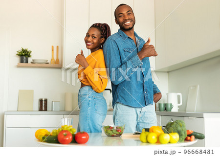 Excited black couple making healthy vegan salad with many vegetables in modern kitchen and showing thumbs up 96668481