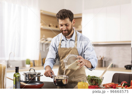 Smiling handsome adult caucasian male chef with beard in apron prepare porridge and salad in modern kitchen Smiling handsome adult caucasian male chef with beard in apron prepare porridge and salad in modern kitchen 96668575