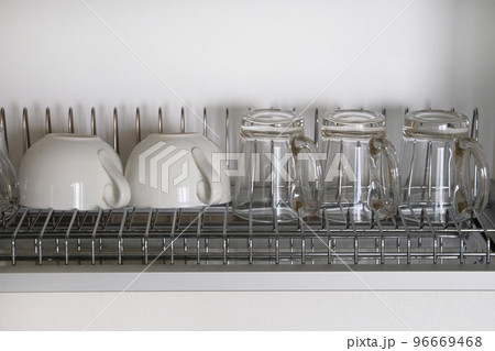 White washed glass and ceramic cups on metal rack inside kitchen cupboard. Modern kitchen with tableware drying 96669468