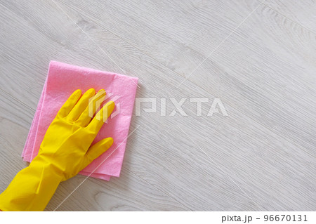 Cleaning concept in office, home. Hand in yellow rubber protective glove with micro fiber cloth is cleaning wooden floor. Copy space. 96670131