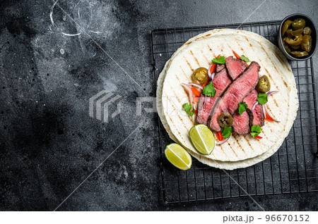 Grilled Beef steak Fajitas, taco tortillas with onion, jalapeno and bell pepper. Black background. top view. copy space Grilled Beef steak Fajitas, taco tortillas with onion, jalapeno and bell pepper. Black background. top view. copy space 96670152