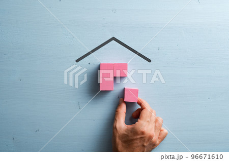 Male hand assembling a house made of pink wooden blocks over blue background 96671610