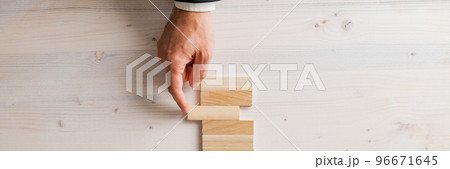 Top view of male hand in a suit pushing a blank wooden peg into a stack of them Top view of male hand in a suit pushing a blank wooden peg into a stack of them 96671645