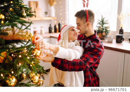 Happy couple decorating christmas tree at home. Smiling Man and Woman together Celebrating Christmas Happy couple decorating christmas tree at home. Smiling Man and Woman together Celebrating Christmas 96671701