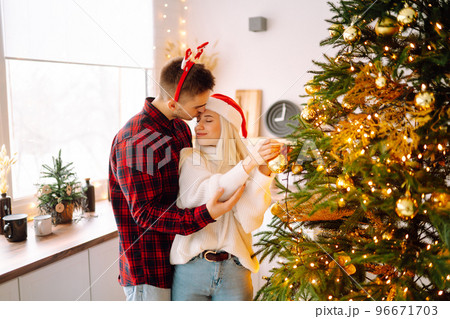 Happy couple decorating christmas tree at home. Smiling Man and Woman together Celebrating Christmas Happy couple decorating christmas tree at home. Smiling Man and Woman together Celebrating Christmas 96671703