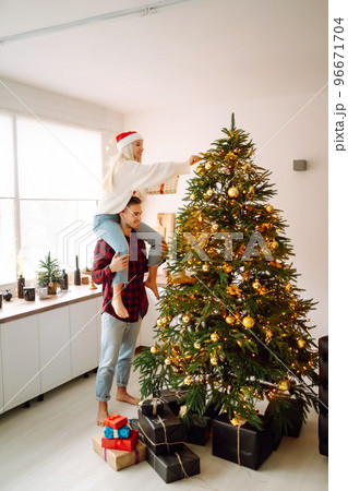 Happy couple decorating christmas tree at home. Smiling Man and Woman together Celebrating Christmas Happy couple decorating christmas tree at home. Smiling Man and Woman together Celebrating Christmas 96671704