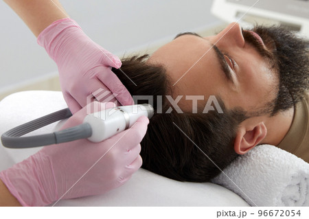 Doctor female dermatologist trichologist makes a procedure to stimulate hair growth on head to a patient man Doctor female dermatologist trichologist makes a procedure to stimulate hair growth on head to a patient man 96672054