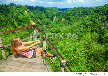 Woman sit at balcony on high cliff with jungle view 96673264