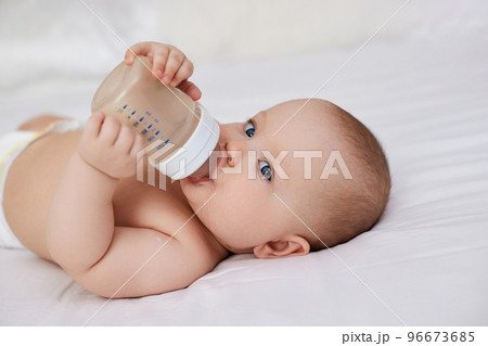 baby girl lies in bed and drinks water from a bottle 96673685