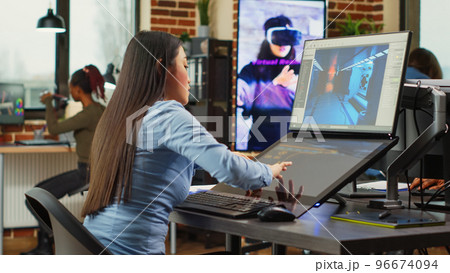 Female artistic editor working on gaming production to create professional content, using touchscreen display. Expert developing 3D scenes and creative graphics on professional software. 96674094