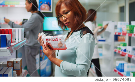 Pharmacy client reading cardiology drugs boxes on shelves, searching for healthcare medicine. Female customer checking pharmaceutics package in drugstore, medical supplies and vitamins. Pharmacy client reading cardiology drugs boxes on shelves, searching for healthcare medicine. Female customer checking pharmaceutics package in drugstore, medical supplies and vitamins. 96674095