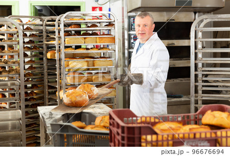 Bakery worker pulling loaves from oven Bakery worker pulling loaves from oven 96676694