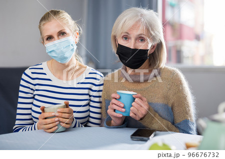Two women in protective mask drink tea 96676732
