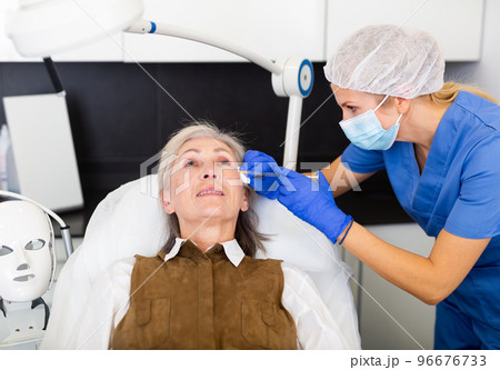 Professional beautician performing face contouring injections to aged woman 96676733