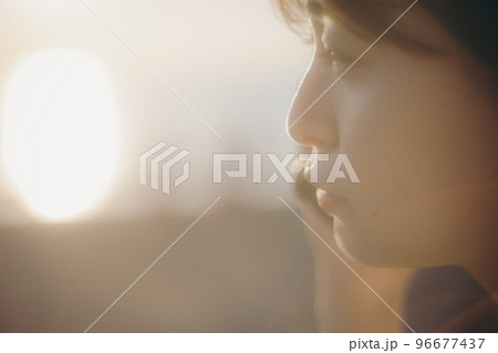 夕日をバックにスマホを持つ女性の写真 96677437