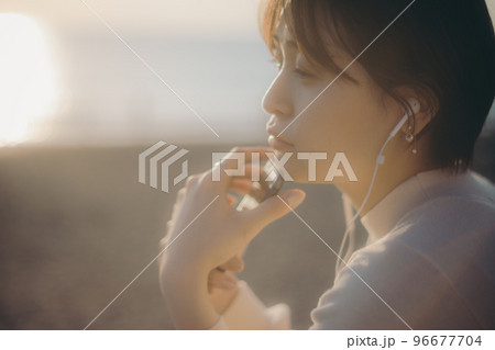 夕日をバックにスマホで音楽を聴く若い女性の写真 夕日をバックにスマホで音楽を聴く若い女性の写真 96677704