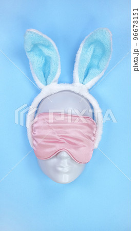 Pink sleeping eye mask on mannequin face with blue fluffy Easter bunny ears on blue background, sleeping disorder. Holidays, Head accessory. Plastic face. Pink sleeping eye mask on mannequin face with blue fluffy Easter bunny ears on blue background, sleeping disorder. Holidays, Head accessory. Plastic face. 96678151