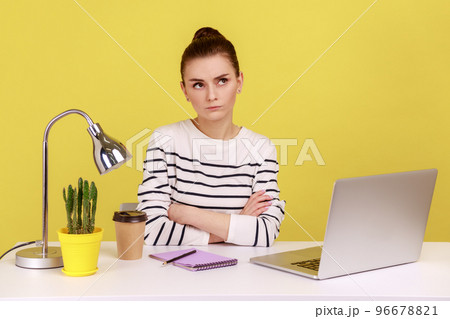 Pensive puzzled woman in striped shirt sitting with thoughtful confused expression while working on laptop in office, thinking over project. Indoor studio studio shot isolated on yellow background. Pensive puzzled woman in striped shirt sitting with thoughtful confused expression while working on laptop in office, thinking over project. Indoor studio studio shot isolated on yellow background. 96678821