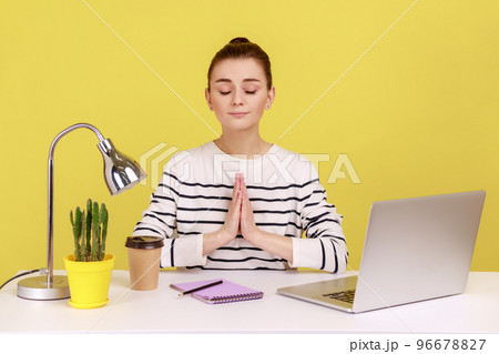 Open minded woman office worker in striped shirt pressing hands together meditating at workplace, preparing herself for work. Indoor studio studio shot isolated on yellow background. 96678827