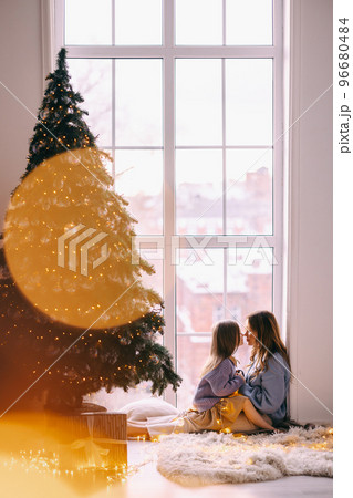 Mother and daughter sitting on the floor by the window Mother and daughter sitting on the floor by the window 96680484