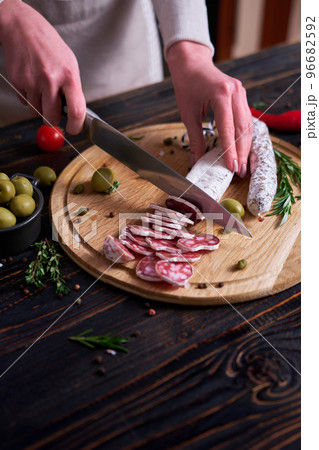 Woman slicing Spanish fuet salami sausageon wooden cutting board at domestic kitchen 96682592