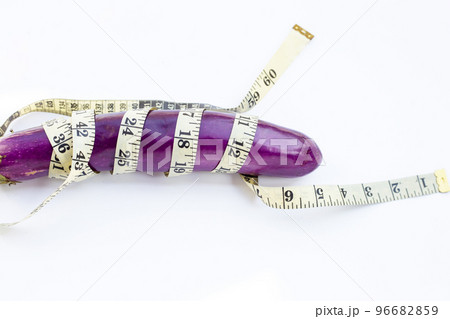 Long purple eggplant wrapped in measuring tape on white background. Long purple eggplant wrapped in measuring tape on white background. 96682859