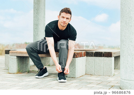 スニーカーの靴紐を結んで運動の準備をするスポーツウェアを着た白人男性 96686876