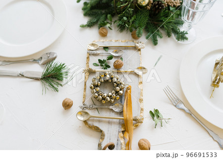 Top view of a festive Christmas table setting on a white background with a decorated pine branch, glass cutting Board, and a wreath of bells 96691533