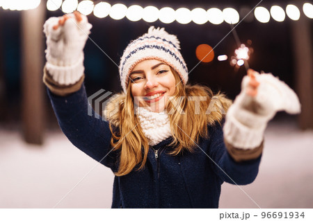 Cheerful young woman holding a sparkler in hand in the winter forest. Happy cute girl posing with sparkler. 96691934