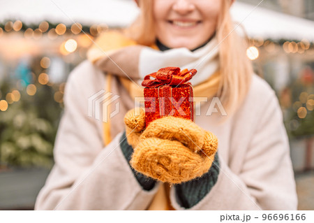Beautiful excited blonde young woman wearing winter clothes standing showing gift box at city street at the Christmas Market in Krakow.  96696166