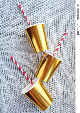 Gold-colored paper cups with striped straw on knitted background for Christmas party decorations, mockup 96696616