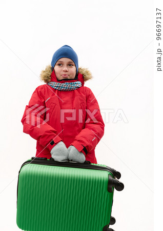 Happy multi-ethnic traveler child boy, wearing warm red down jacket, holding a green suitcase, going for winter vacations, isolated over white background with free advertising space. Kids travelling Happy multi-ethnic traveler child boy, wearing warm red down jacket, holding a green suitcase, going for winter vacations, isolated over white background with free advertising space. Kids travelling 96697137