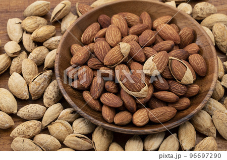 丸い木の皿に盛ったアーモンドと殻付きアーモンド_背景板 96697290