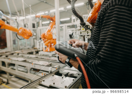 Technical engineer adjusting a robotic arm in the industrial automotive hall, industry concept Technical engineer adjusting a robotic arm in the industrial automotive hall, industry concept 96698514