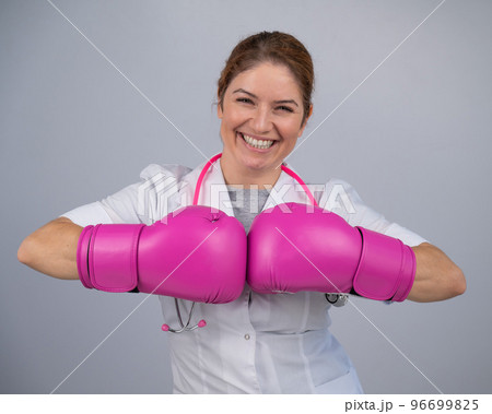 Smiling female doctor in pink boxing gloves with a pink ribbon on a gray background. Fight against breast cancer. Smiling female doctor in pink boxing gloves with a pink ribbon on a gray background. Fight against breast cancer. 96699825