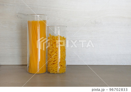 Pasta in large glass jars containers stand on gray table in kitchen. Uncooked raw italian pasta with spaghetti. 96702833