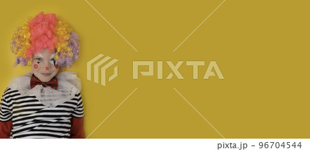 A boy in a clown costume on the background of a bright yellow wall is fooling around and smiling A boy in a clown costume on the background of a bright yellow wall is fooling around and smiling 96704544