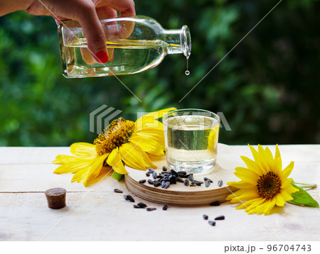 Sunflower oil pouring from the bottle into a glass with sunflowers and seeds on background Sunflower oil pouring from the bottle into a glass with sunflowers and seeds on background 96704743
