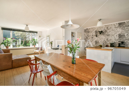 Table with chairs and flowers located near lounge area and kitchen in spacious room of contemporary apartment 96705049